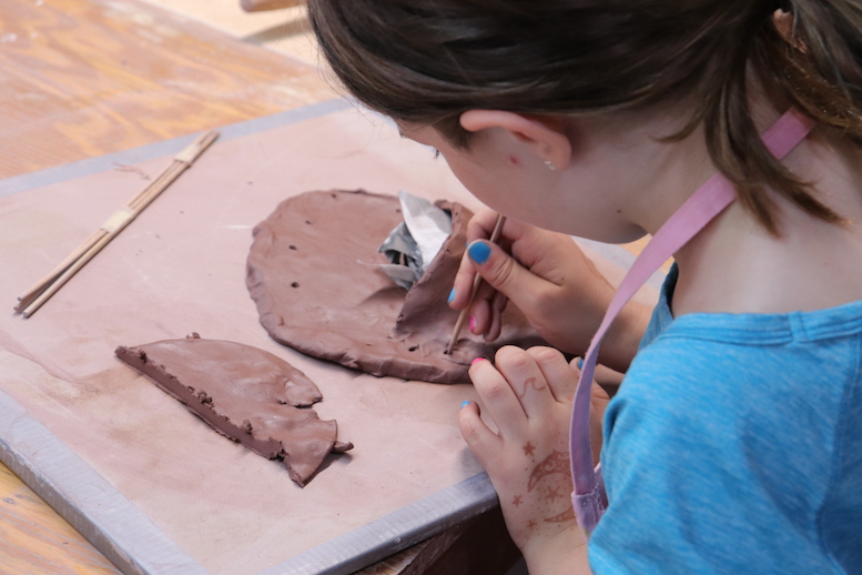 Over the shoulder of a Girl Handbuilding with red clay