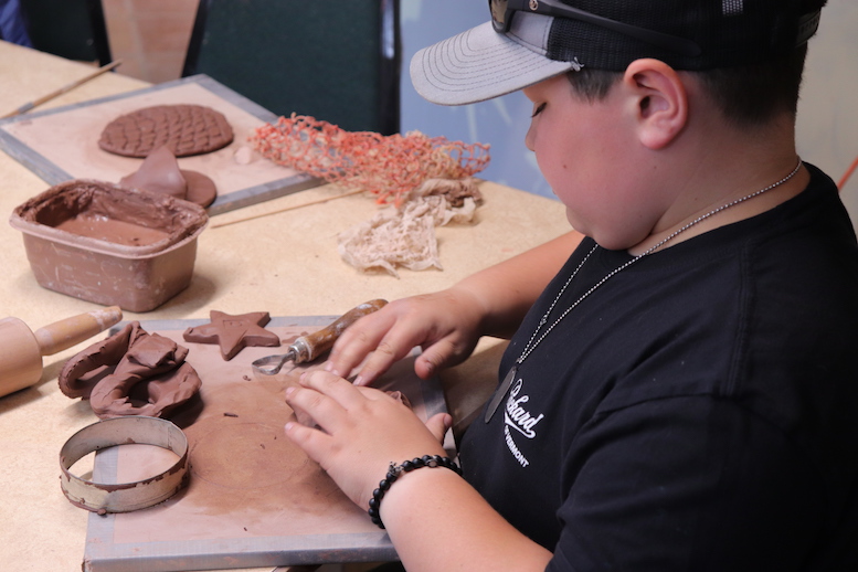 Boy sculpting with red clay in a studio