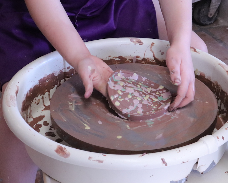 Child's hand taking piece off a potter's wheel decorated with colored slip