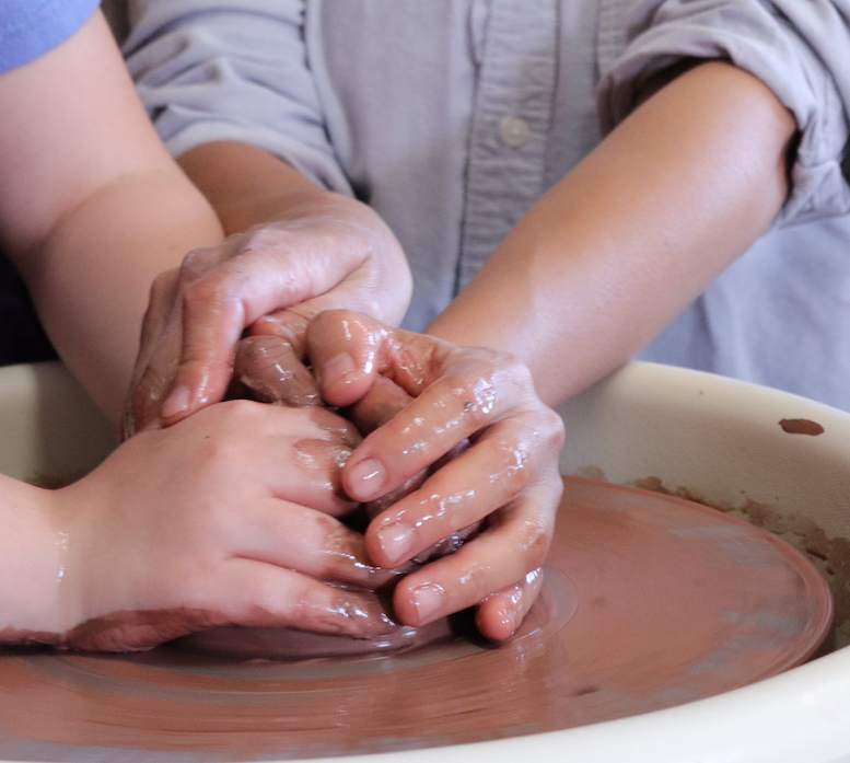 Kids & Adult hands working with red clay on a potter's wheel
