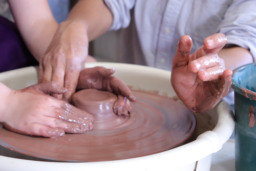 Adult & Kids hands working with red clay on a potter's wheel