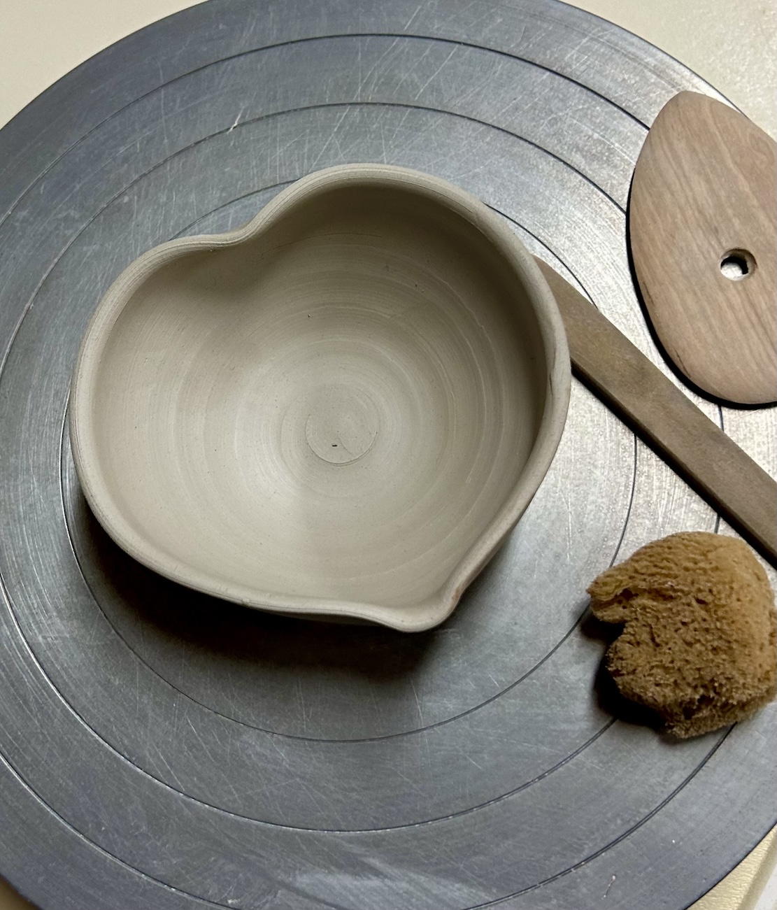 heart shaped clay bowl on a potter's wheel with tools