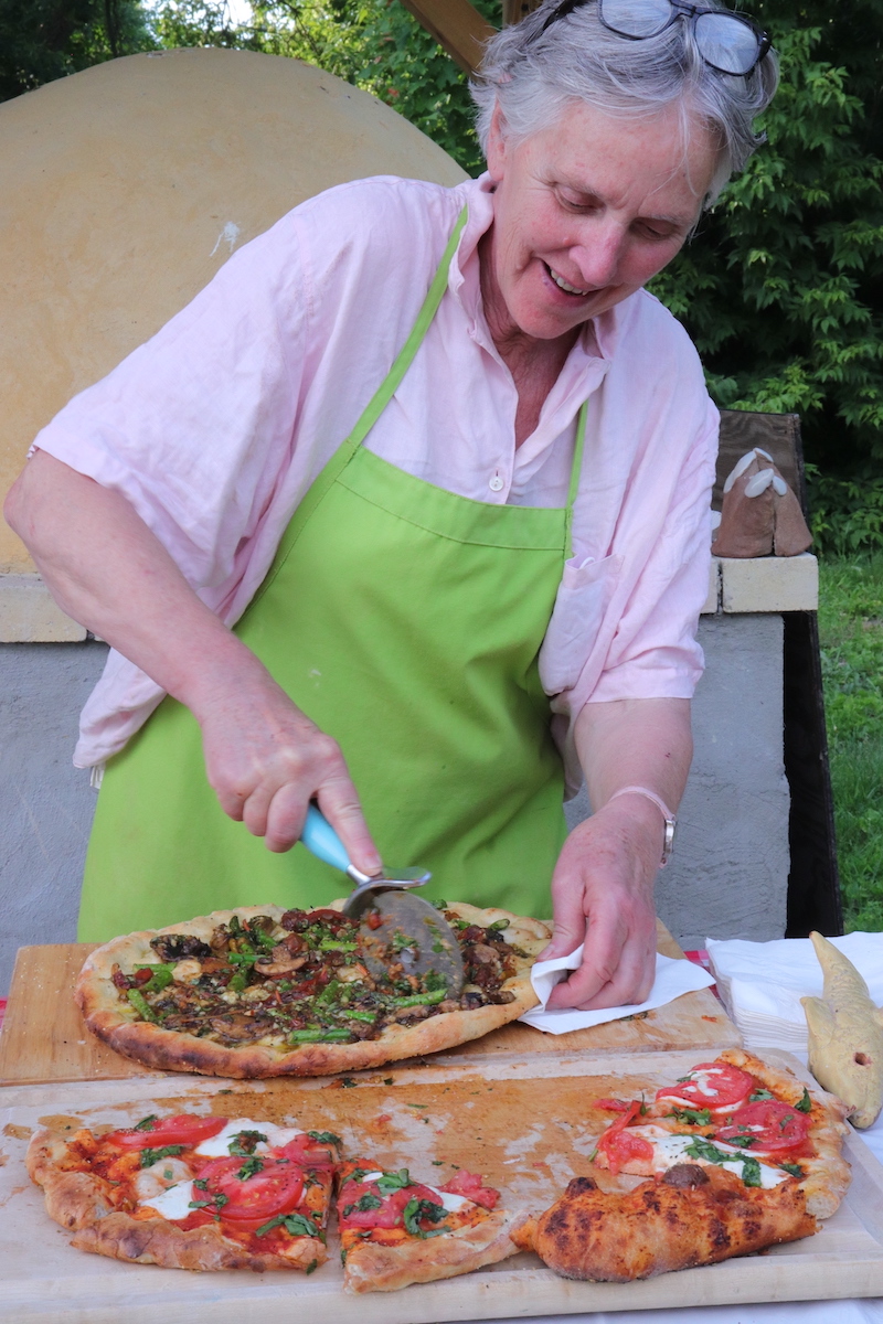 Woman slicing wood fired pizza outside