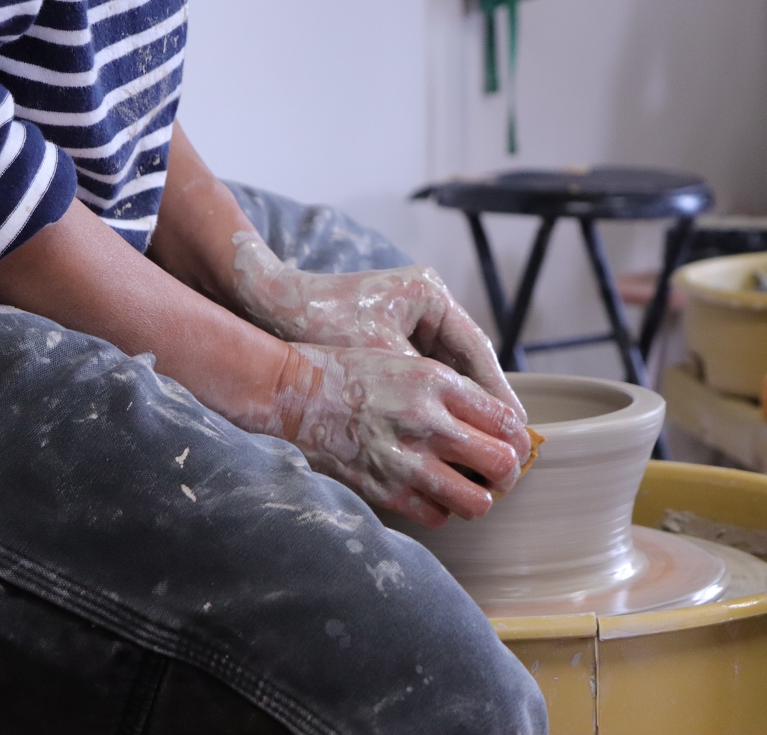 person throwing clay piece on potter's wheel